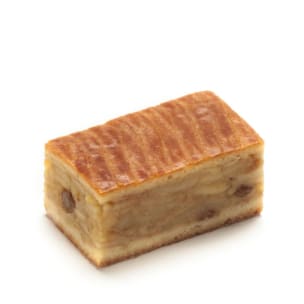 Ein rechteckiges Stück geschichteter Apfelkuchen mit goldbrauner, glänzender Oberfläche und sichtbaren Apfel- und Rosinenstücken im Inneren, vor einem schlichten weißen Hintergrund.