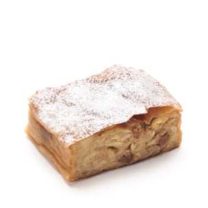 Ein Stück Apfelstrudel mit goldbrauner Blätterteigkruste, bestäubt mit Puderzucker, fotografiert auf weißem Hintergrund.