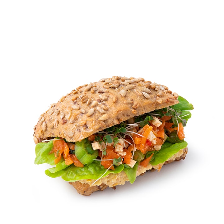 Ein Sandwich auf Mehrkornbrot mit Sonnenblumenkernen, gefüllt mit Salat, Sprossen, Gemüsewürfeln und etwas, das aussieht wie zerbröckelter Tofu oder Tempeh, auf weißem Hintergrund.