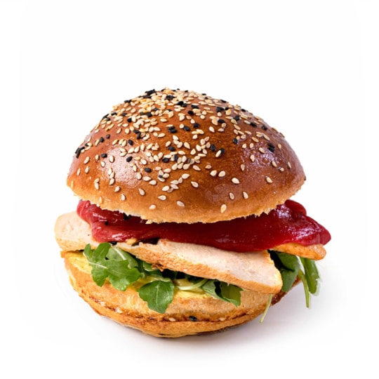 Ein Sesambrötchen, gefüllt mit gegrillter Hähnchenbrust, Rucola, gerösteter roter Paprika und einer Schicht Sauce, auf weißem Hintergrund.