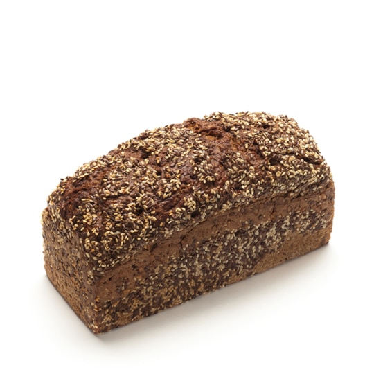 Ein ganzer Laib dunkles, entkörntes Brot ist auf einem weißen Hintergrund abgebildet. Das Brot ist rechteckig mit einer abgerundeten Spitze und ist mit verschiedenen Samen bedeckt.