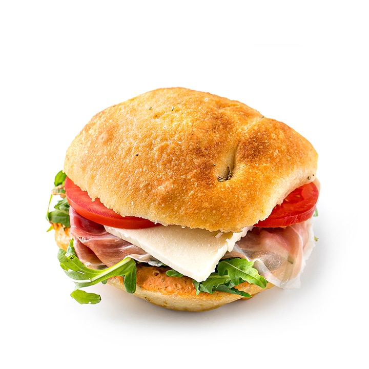 Ein Sandwich mit Prosciutto, Rucola, Tomatenscheiben und einer Scheibe Käse auf einem rustikalen Brötchen, vor einem weißen Hintergrund.