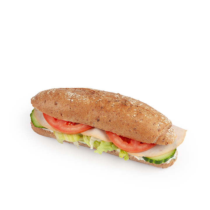 Ein Vollkornsandwichbrötchen, gefüllt mit Salat, Tomatenscheiben, Gurken und Wurstwaren, dargestellt auf weißem Hintergrund.