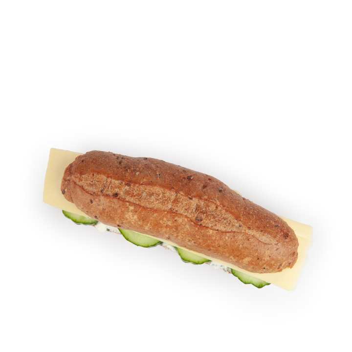 Ein Vollkornsandwichbrötchen, gefüllt mit Käsescheiben, Gurken und einer Schicht weißem Aufstrich, von oben auf weißem Hintergrund fotografiert.