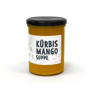 Ein Glasgefäß mit schwarzem Deckel, gefüllt mit orangefarbener Suppe. Auf dem Etikett steht "Kürbis Mango Suppe" mit kleinen Samenabbildungen um den Text herum.