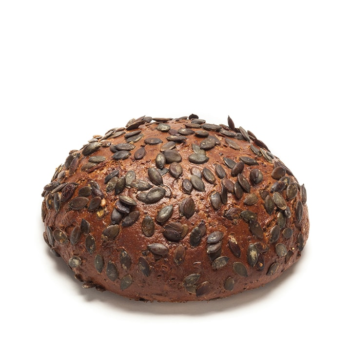 Ein runder Laib dunkelbraunes Brot mit zahlreichen Kürbiskernen auf einem schlichten weißen Hintergrund.
