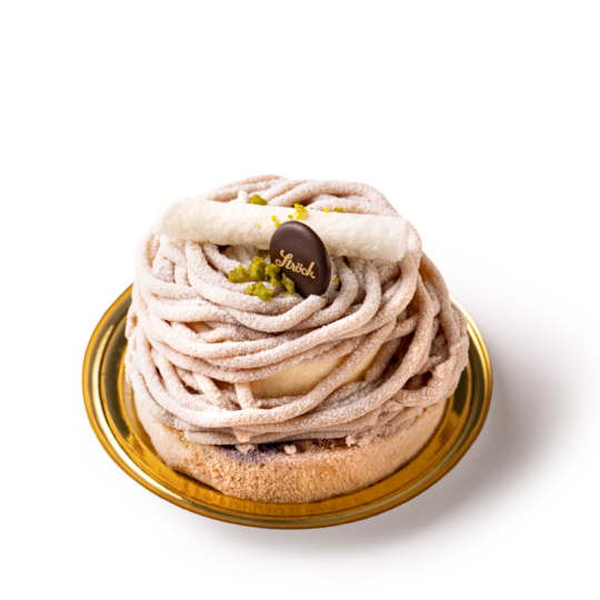 Ein rundes Mont-Blanc-Dessert mit Kastaniencreme in Strudeln, bestäubt mit Puderzucker, gekrönt mit einer weißen Baiserstange, einer Schokoladentafel und zerstoßenen Pistazien, auf einem goldenen Teller vor weißem Hintergrund.