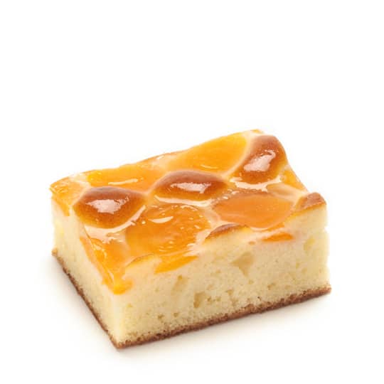 Eine rechteckige Kuchenscheibe mit glänzenden Mandarinensegmenten auf einem leichten, flauschigen Biskuitboden vor einem schlichten weißen Hintergrund.