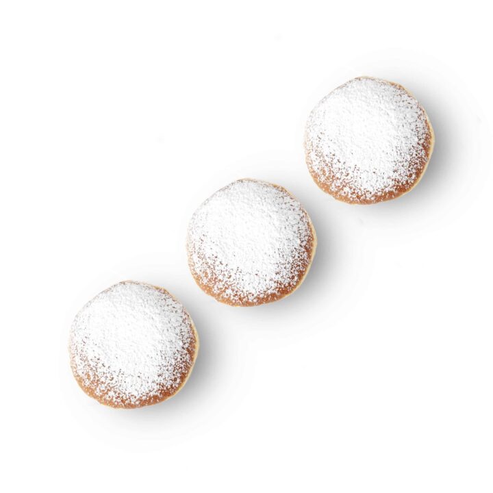 Drei runde, mit Puderzucker bestäubte Gebäckstücke sind diagonal auf einem weißen Hintergrund angeordnet.