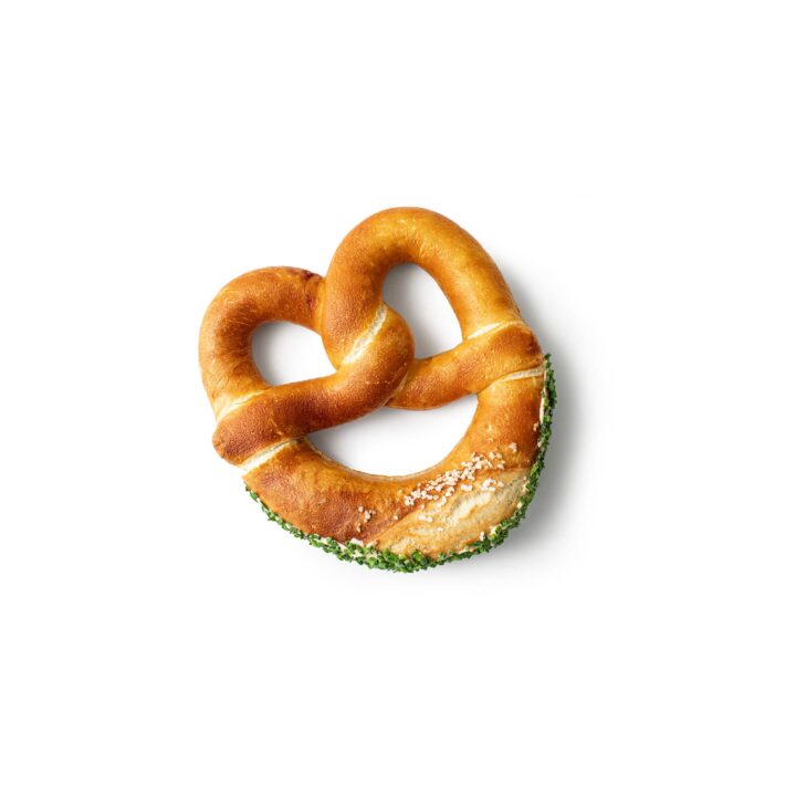 Eine goldbraune Brezel, bestreut mit Sesam und gehackten grünen Kräutern auf einer Seite, isoliert auf einem weißen Hintergrund.