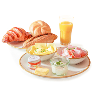 Ein Frühstücksaufstrich mit einem Croissant, Brötchen, einem Glas Orangensaft, Käsescheiben, Schinken, einem Glas Marmelade, einem Stück Butter und einem kleinen Glas Frischkäse, garniert mit gehacktem Schnittlauch.