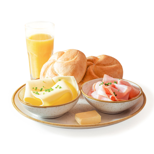 Ein Frühstücksteller mit zwei Brötchen, einer Schüssel mit Käsescheiben und Schnittlauch, einer Schüssel mit Schinkenscheiben, einem kleinen Stück Butter und einem Glas Orangensaft, alles auf weißem Hintergrund.