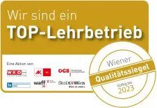 Goldenes Abzeichen mit dem Text Wir sind ein TOP-Lehrbetrieb und Wiener Qualitätssiegel gültig bis 2023, mit Logos österreichischer Organisationen am unteren Rand.
