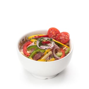 Eine weiße Schale mit einem frischen Salat, der Tomatenscheiben, rote Zwiebeln, grüne und gelbe Paprika und Kräuter enthält.