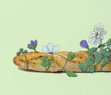 Ein Baguette liegt auf einer blassgrünen Fläche, um die sich illustrierte Blumen und Kleeblätter ranken, die reale und gezeichnete Elemente in einer skurrilen Komposition vereinen.