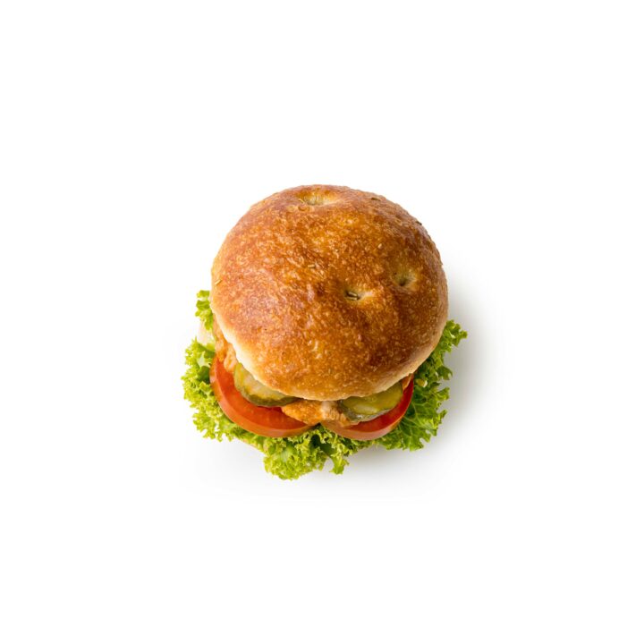 Ein rundes Sandwich mit goldbraunem Brötchen, grünem Blattsalat, Tomatenscheiben und anderen Füllungen, abgebildet auf einem weißen Hintergrund.