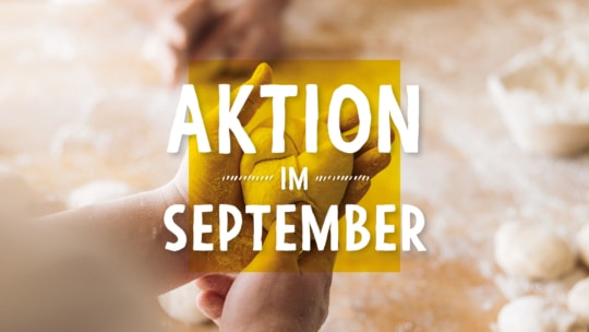 Eine Person formt mit mehligen Händen Teig auf einer Holzfläche. Der Text AKTION IM SEPTEMBER ist in fetten weißen Buchstaben auf gelbem Hintergrund überlagert.