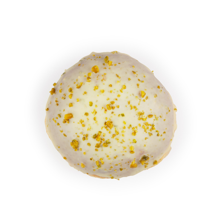 Ein runder, mit weißem Zuckerguss überzogener und mit zerstoßenen Pistazien bestreuter Kuchen, fotografiert von oben auf weißem Hintergrund.