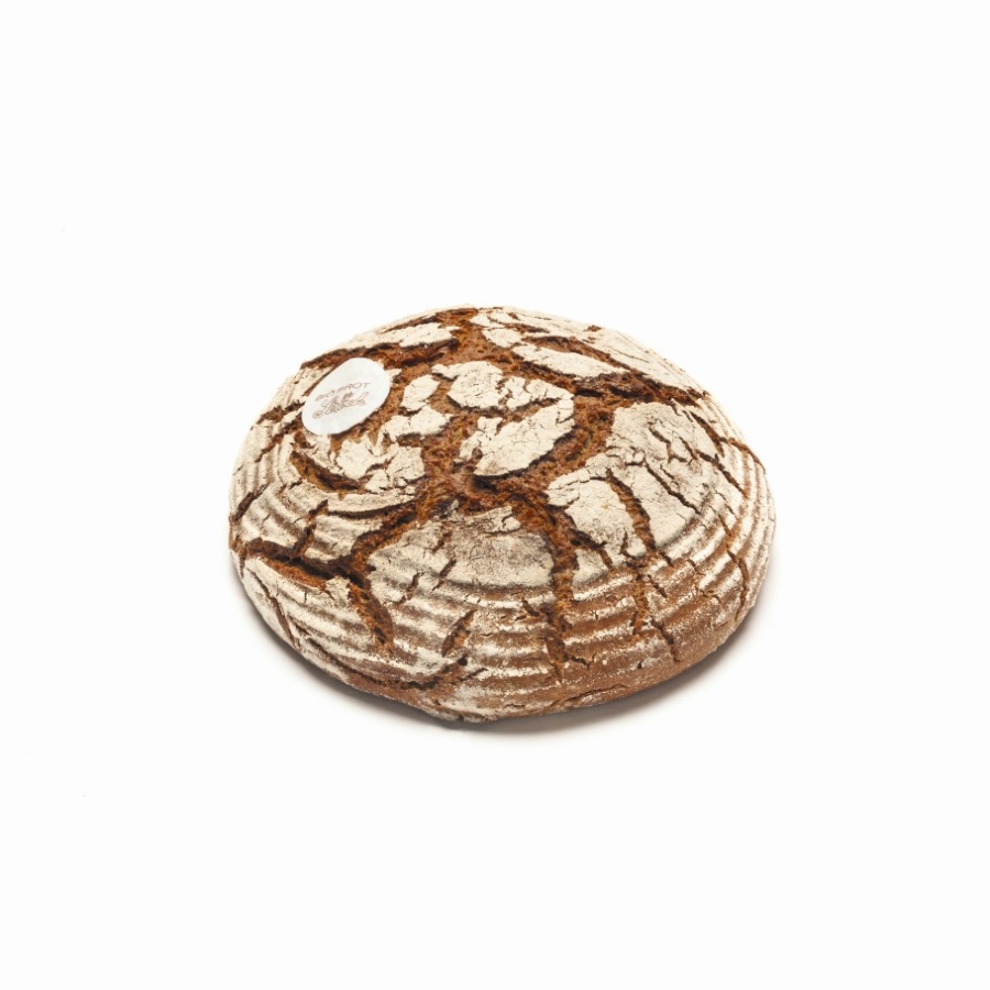 Ein runder Laib rustikales, handwerklich hergestelltes Brot mit einer rissigen, mehlbestäubten Kruste liegt auf einem weißen Hintergrund. Ein kleines weißes Etikett ist an der oberen linken Seite des Laibes angebracht.