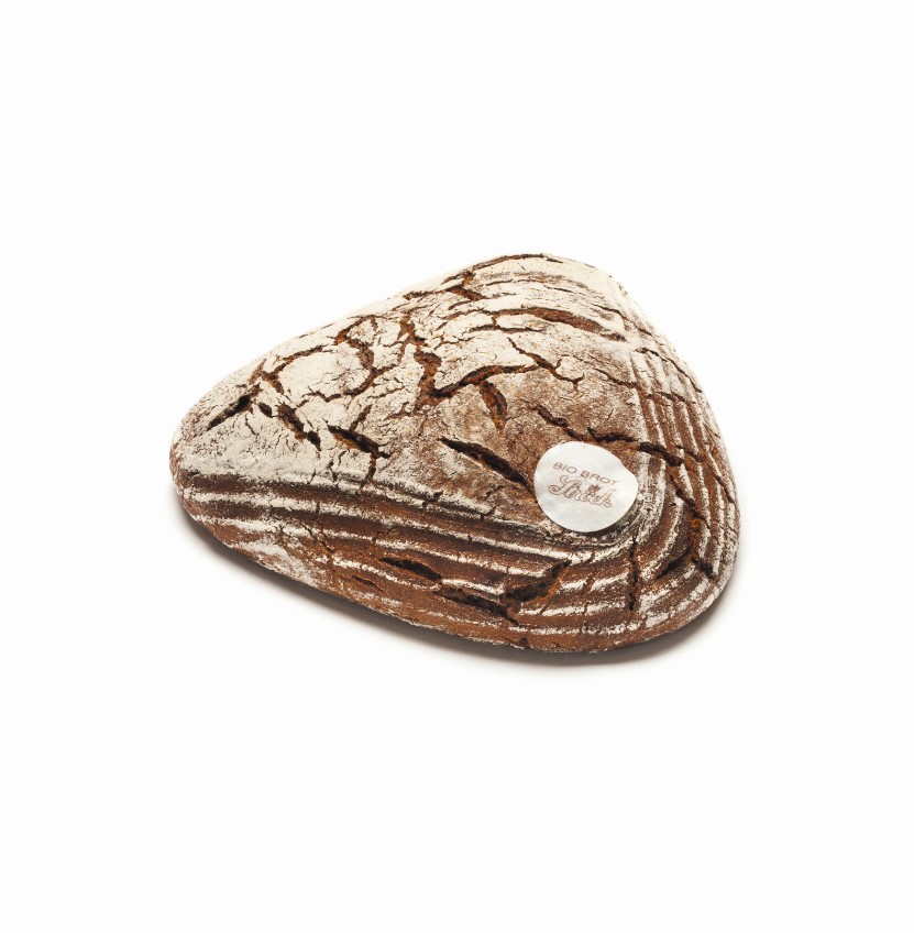 Ein dreieckiger Laib rustikalen Brotes mit einer rissigen, mehlbestäubten Kruste liegt auf einem weißen Hintergrund. Ein kleines rundes Etikett befindet sich oben auf dem Laib.