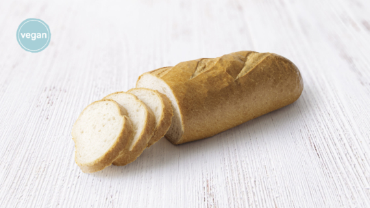 Ein in Scheiben geschnittener Laib Weißbrot liegt auf einer hellen Holzfläche. Ein blauer Kreis in der Ecke zeigt das Wort "vegan" an und weist darauf hin, dass das Brot veganfreundlich ist.