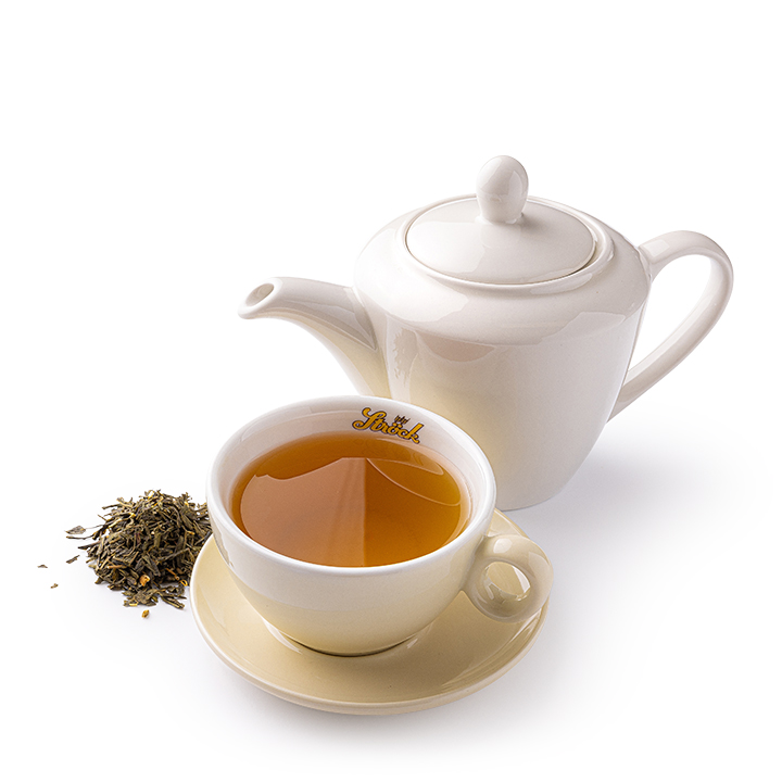 Eine weiße Teekanne und eine mit Tee gefüllte Teetasse stehen auf einer weißen Untertasse. Lose Teeblätter sind neben der Tasse und der Kanne verstreut, alles vor einem weißen Hintergrund.