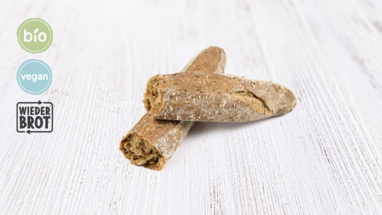 Zwei Stücke rustikales Baguette-Brot auf einer weißen Holzunterlage, mit den Logos von Bio, Vegan und Wieder Brot auf der linken Seite des Bildes.
