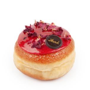 Ein runder, glasierter Donut mit leuchtend rotem Zuckerguss, getrockneten Rosenblättern und einer kleinen Schokoladenscheibe mit goldener Schrift vor einem schlichten weißen Hintergrund.