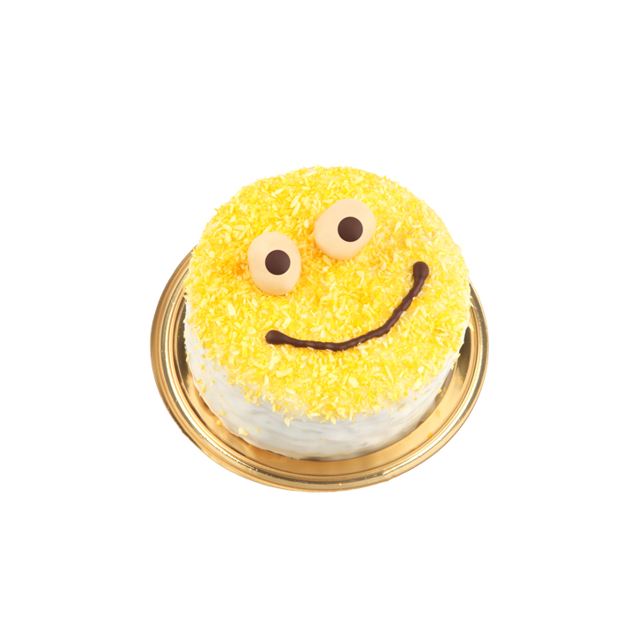 Eine runde Torte, verziert mit gelben Streuseln und einem Smiley-Gesicht aus Schokolade und runden Bonbons, auf einer goldumrandeten Platte vor weißem Hintergrund.