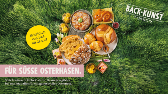 Ein Teller mit verschiedenen Ostergebäcken, Eiern und Getränken steht auf grünem Gras. Auf einem gelben Etikett steht Erhältlich von 10.4. bis 21.4.25. Der Text darunter lautet Für süße Osterhasen. und Ostergrüße auf Deutsch.