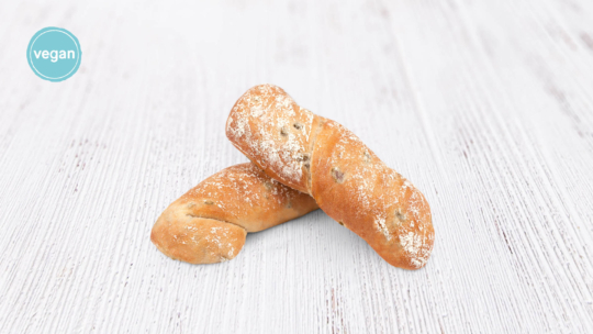Zwei rustikale, mit Mehl bestäubte Brotstücke liegen auf einer weißen Holzfläche. Ein blauer Kreis in der oberen linken Ecke zeigt das Wort "vegan".