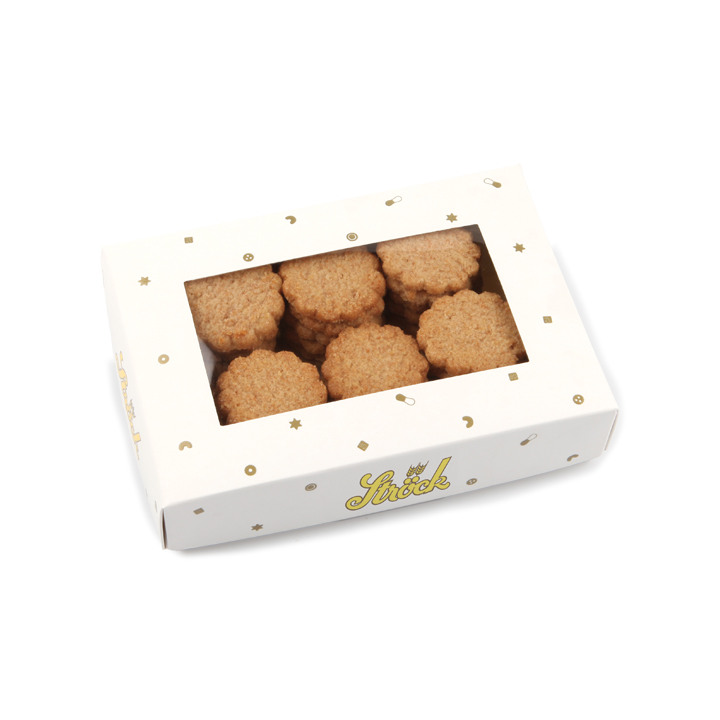 Eine weiße Schachtel mit einem durchsichtigen Fenster auf der Oberseite, in dem mehrere runde, goldbraune Kekse zu sehen sind. Auf der Schachtel sind goldene Ziersymbole und das Wort Ströck aufgedruckt.