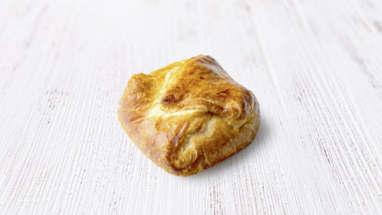 Ein goldbrauner Blätterteig mit einer gefalteten, quadratischen Form liegt auf einer hellen Holzunterlage.