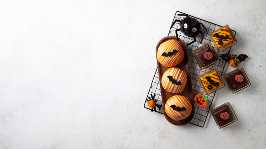 Gebäck und Pralinen zum Thema Halloween, verziert mit Fledermäusen und Kürbissen, auf einem Abkühlgitter, dazu eine flauschige Spinnenverzierung.