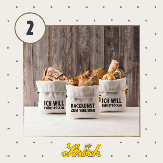 Three fabric bread bags filled with assorted breads sit on a light surface. The bags have German text, and a number 2 is in a circle at the top left. The background has a wooden panel and confetti-like decorations.