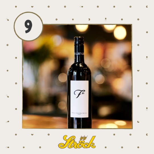 A bottle of red wine labeled F 01 is centered on a blurred bar background. The image has a beige border with small decorative shapes, a circle with the number 9, and the Ströck logo at the bottom.