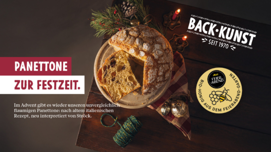 A festive table with a round panettone on a wooden board, decorated with powdered sugar and almonds. Holiday decorations and twine are nearby. German text promotes Stöck’s panettone for the Christmas season.