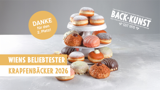 Auf einem mehrstöckigen Kuchenständer stehen verschiedene Donuts und Gebäckstücke, einige mit Puderzucker, Zuckerguss oder Schokolade. Der Text lautet: Wiens beliebtester Krapfenbäcker 2026 und Danke für den 2. Platz! mit dem Logo von Back Kunst seit 1970.