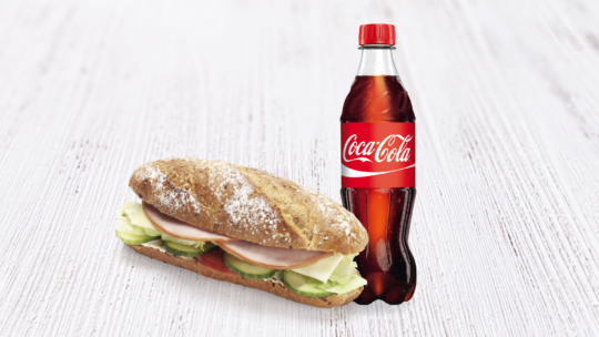 Ein Sandwich mit Salat, Tomate, Gurke und Wurst auf einem knusprigen Brötchen steht neben einer Flasche Coca-Cola auf einer hellen Holzfläche.