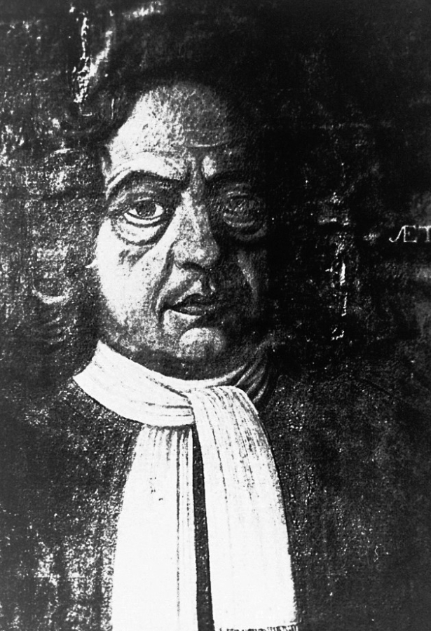 Schwarz-Weiß-Porträt eines Mannes mit lockigem Haar, der einen dunklen Mantel und ein weißes Halstuch trägt und den Betrachter direkt anschaut. Der Hintergrund ist dunkel und undeutlich, mit einem teilweise sichtbaren Text auf der rechten Seite.