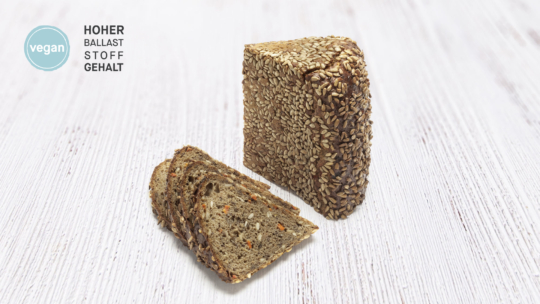 Abgebildet ist ein mit Körnern bestreutes Mehrkornbrot, von dem vorne drei Scheiben abgeschnitten sind. Ein blaues veganes Etikett und der deutsche Text HOHER BALLASTSTOFFGEHALT erscheinen auf der linken Seite.