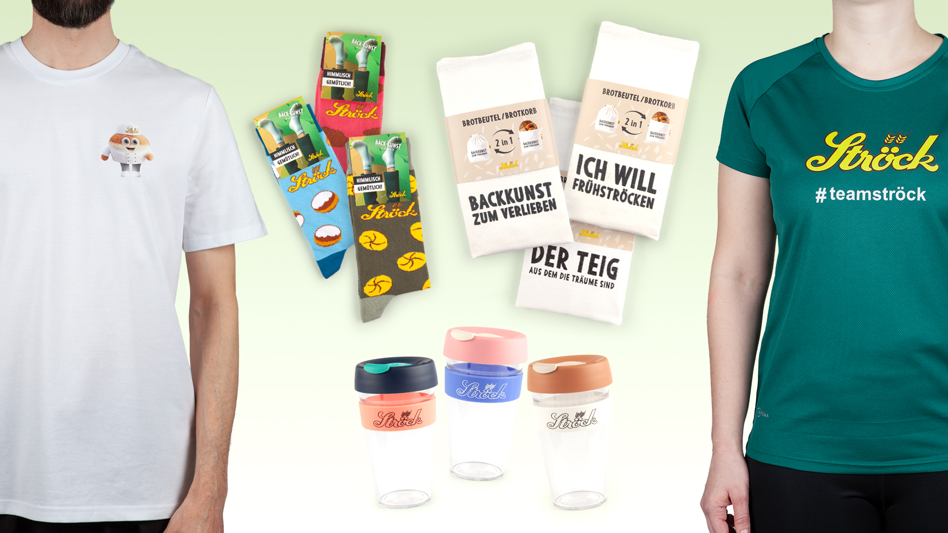 Zwei Personen tragen Ströck Markenhemden, umgeben von bunten Ströck-Socken, zwei weißen Küchentüchern mit deutscher Aufschrift und drei wiederverwendbaren Kaffeebechern mit rosa, blauen und beigen Deckeln.