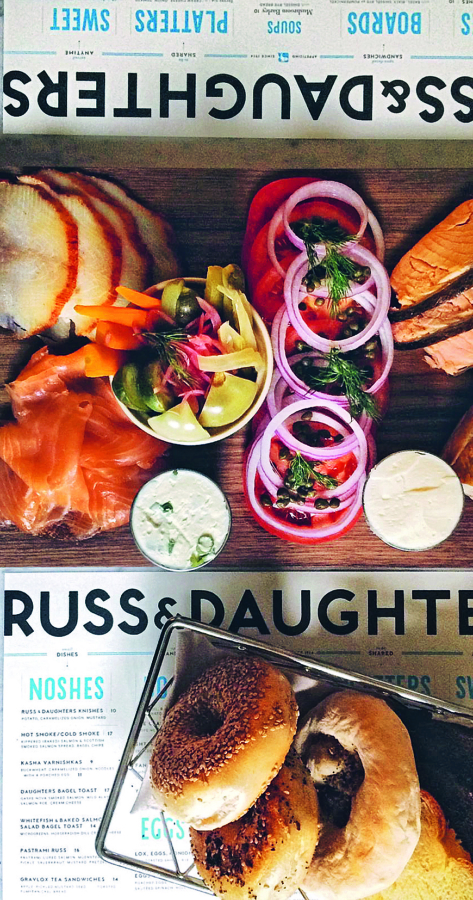Eine Platte mit geräuchertem Fisch, geschnittenen roten Zwiebeln, Tomaten, Gurken, Kapern, Essiggurken, Frischkäse und Bagels auf einer Matte der Marke Russ & Daughters.