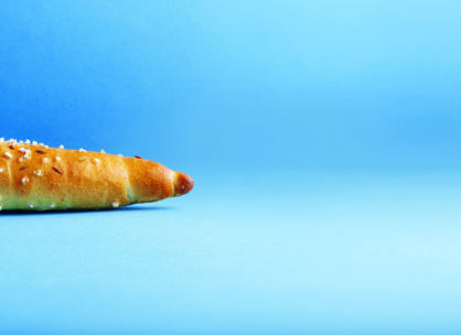 Ein mit Sesamsamen belegtes Brötchen liegt auf einer flachen blauen Fläche, wobei nur der linke Teil des Brötchens vor einem einfarbigen blauen Hintergrund zu sehen ist.