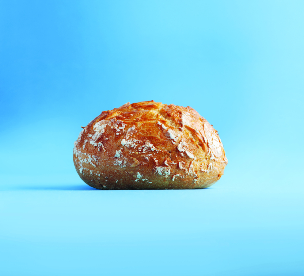 Ein runder, knuspriger Brotlaib mit einer goldbraunen, strukturierten Oberfläche liegt auf einem hellblauen Hintergrund.
