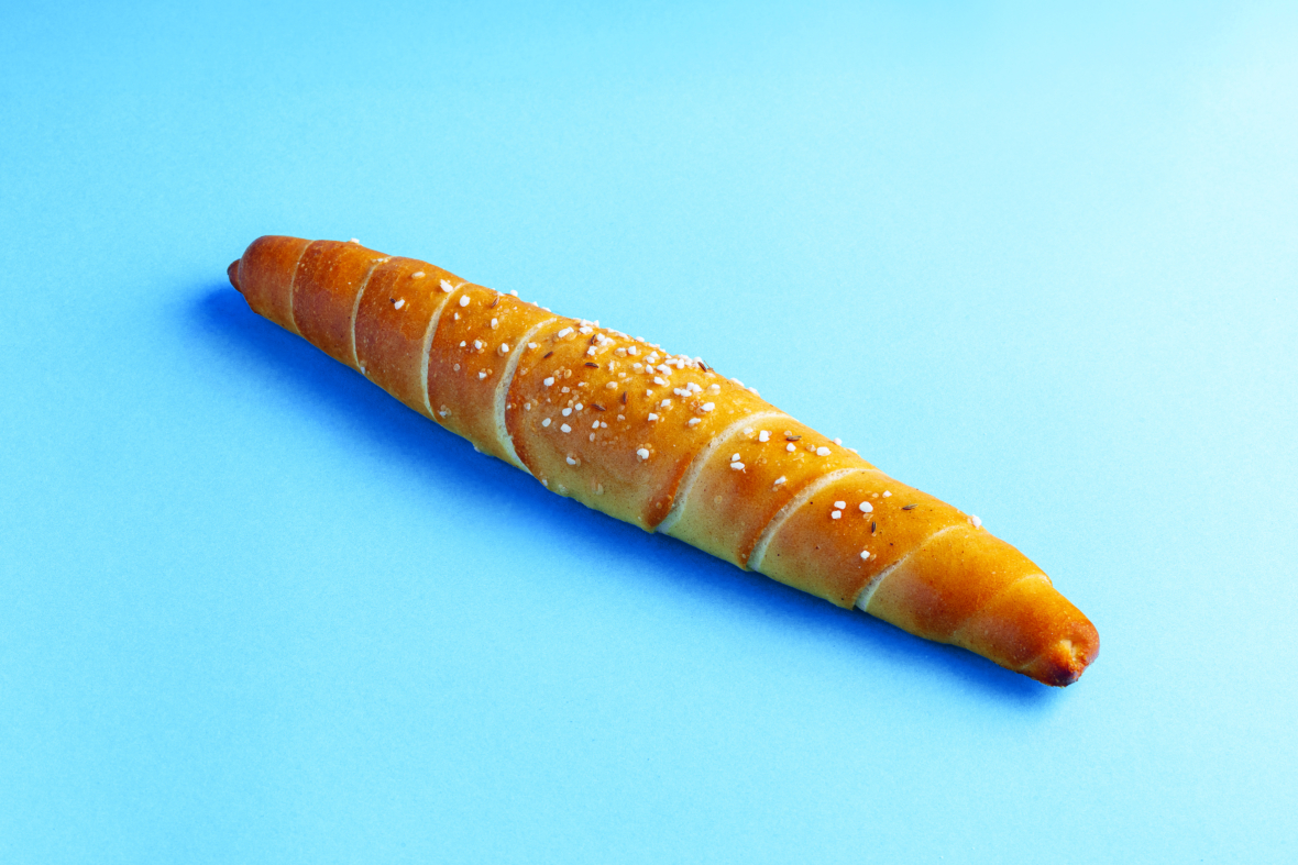 Ein einzelnes goldbraunes, mit grobem Salz bestreutes Brötchen in Form eines langen, gedrehten Horns ist auf einem hellblauen Hintergrund platziert.