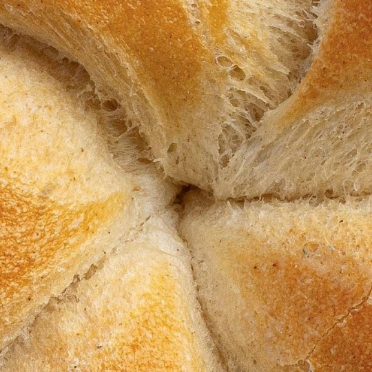 Nahaufnahme eines goldbraunen Brötchens, das die strukturierte Kruste und das weiche, luftige Innere mit den gebogenen Abschnitten zeigt, die sich in der Mitte treffen.