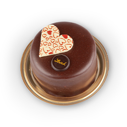 Ein runder Schokoladenkuchen auf einem goldenen Tablett, gekrönt von einem weißen Schokoladenherz, verziert mit roten Herzen und einer kleinen Schokoladenscheibe mit goldener Schrift.