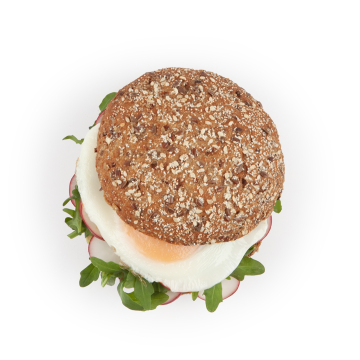 Draufsicht auf ein Sandwich mit einem Mehrkornbrötchen, einem Spiegelei, grünem Blattgemüse und dünnen Radieschenscheiben auf einem weißen Hintergrund.