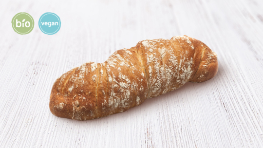 Ein rustikaler Brotlaib im Baguette-Stil auf einer hellen Holzoberfläche, mit Bio- und Vegan-Labels in grünen und blauen Kreisen in der oberen linken Ecke.